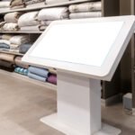 Digital display mock up features a blank screen in a retail environment filled with neatly arranged textiles and blankets, enhancing the shopping atmosphere with copy space